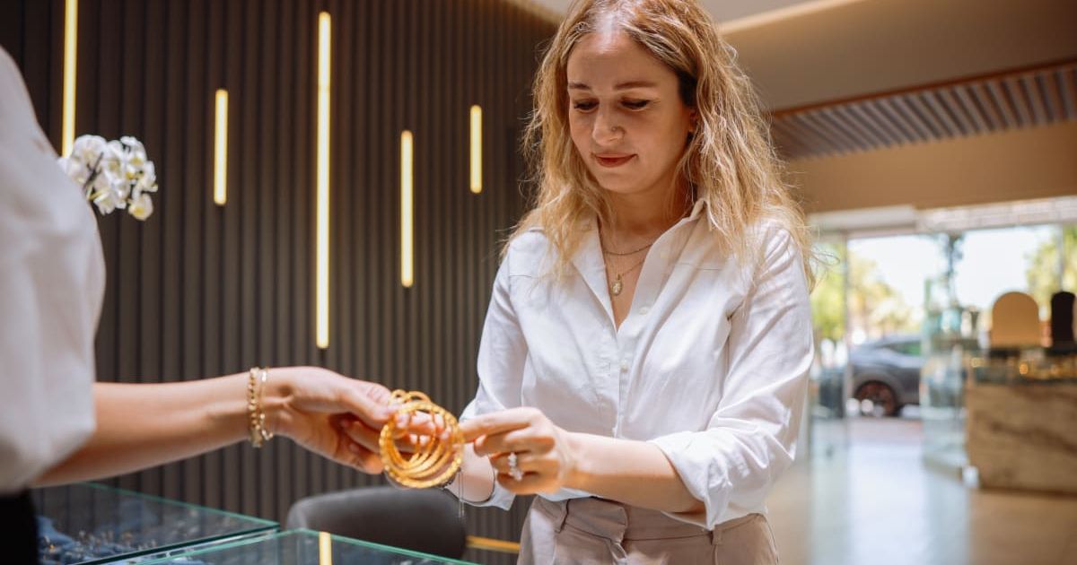 Representative image of a female clerk in a high-end jewelry store trying on a gold bracelet to show to a customer (Cover image source: Getty Images/Photo by  ozgurcankaya)